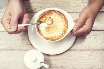 Woman hands with hot cappuccino coffee on a wood table.
