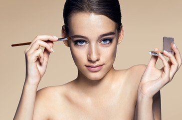 Beautiful woman applying eyeshadow / photos of appealing brunette girl on beige background