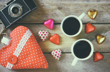 top view image of colorful heart shape chocolates, fabric heart, vintage photo camera and cup of coffee on wooden table. valentine's day celebration concept. retro filtered and toned
