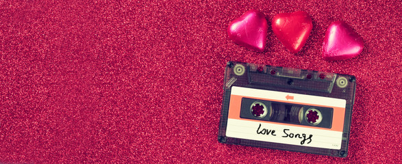 website banner image of colorful heart shape chocolates and audio cassette on glitter  background. valentine's day celebration concept. retro toned and filtered

