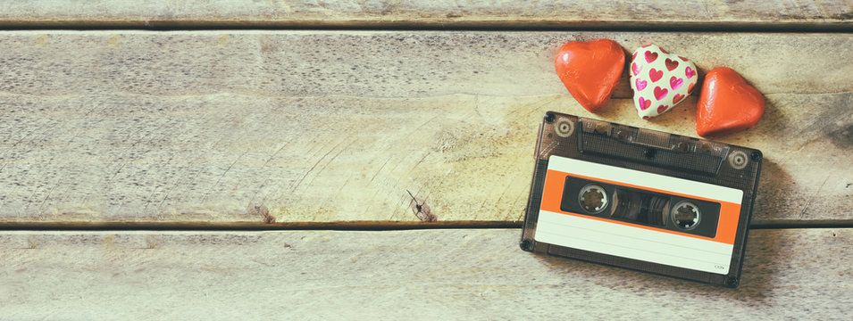 website banner image of colorful heart shape chocolates and audio cassette on wooden table. valentine's day celebration concept. retro toned and filtered
