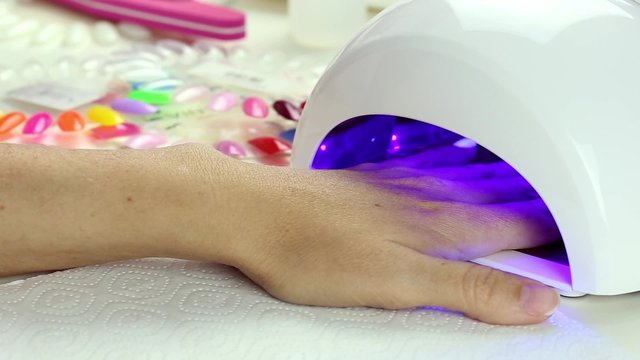 Manicure in process - putting hand and curing gel varnish in nail LED lamp, procedure of polymerization