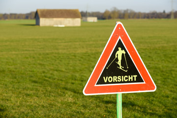 Schild warnt vor Skifahrer auf grüner Wiese wegen Erderwärmung und Klimawandel