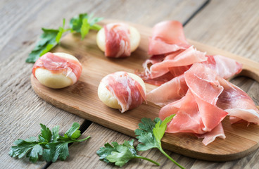 Mini cheese and prosciutto wraps on the wooden board