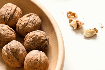 Several whole walnuts in wooden bowl on white background