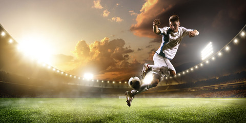 Fototapeta premium Gracz piłki nożnej w akci na zmierzchu stadium panoramy tle