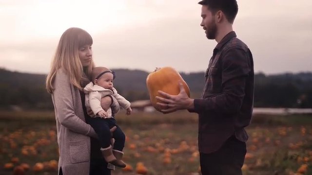 A young father showing a pumpkin to his baby daughter at the pumpkin patch
