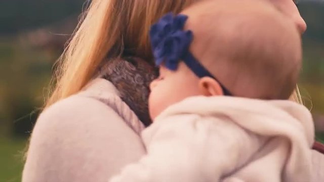 Close up of a mother bouncing her sleepy baby on her shoulder outside on a fall day