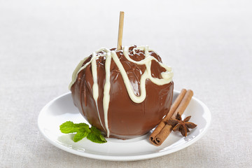 Apple in chocolate on a white plate with mint, cinnamon and anise star