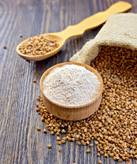 Flour buckwheat in bowl and spoon with cereals on dark board