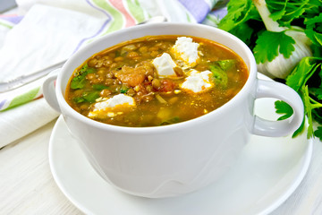 Soup lentil with spinach and feta in white cup on board