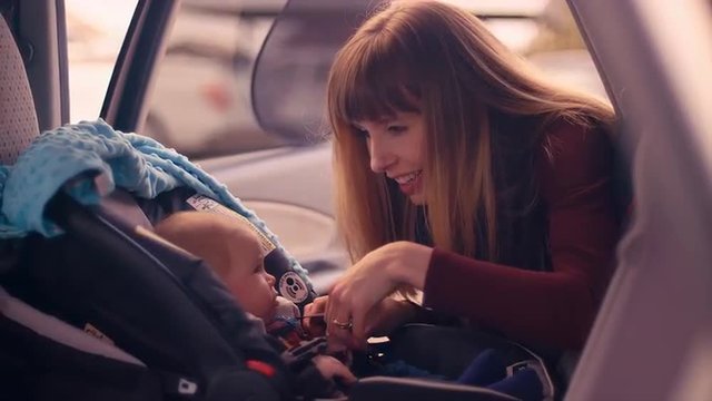 A young mother unbuckling her baby daughter from her car seat