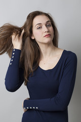 pride and arrogance - pretentious beautiful young girl playing with her hair for seduction and insolence,gray background in studio