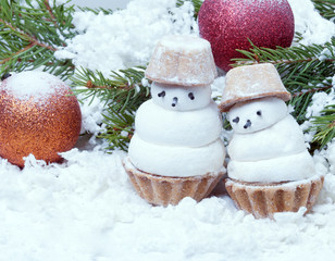 two small snowman and Christmas balls on the branches covered with artificial snow
