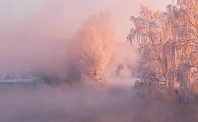 Winter dawn over the misty river, frozen trees illuminated by the red rising sun