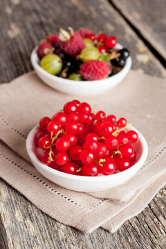 bowl of red currant on wooden background, vertical close-up