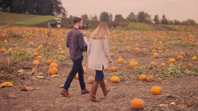 A young couple carrying their baby around at a pumpkin patch