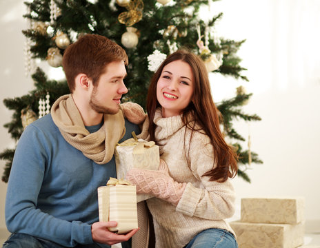 Happy couple with gifts on background of Christmas tree at home