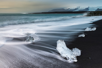 Obrazy na Szkle  Kostka lodu z gładką falą na czarnej, piaszczystej plaży Islandia podczas wschodu słońca