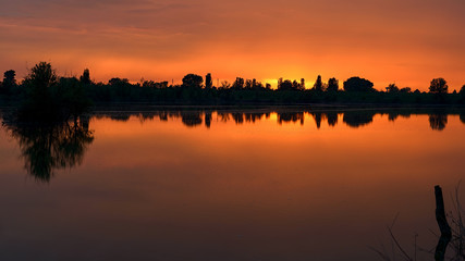 beautiful sunset on the lake with trees reflected in the water