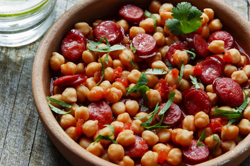 Chickpeas with chorizo in a clay bowl on the table close-up 