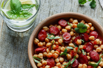 Chickpeas with chorizo in a clay bowl on the table close-up 