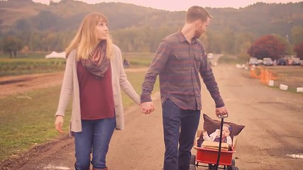A couple walking and holding hands while pulling their baby in a wagon at a pumpkin patch
