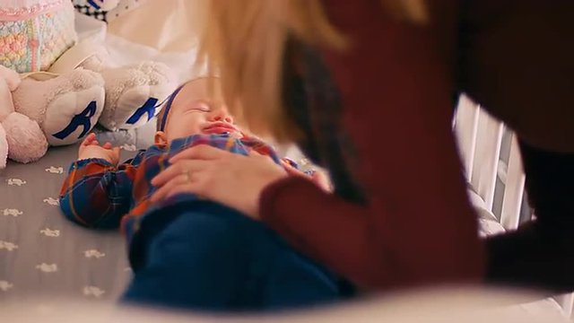 A mother trying to calm her crying baby girl in her crib