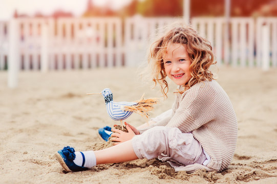 Happy Child Girl Playing With Toy Bird On The Beach On Summer Vacation