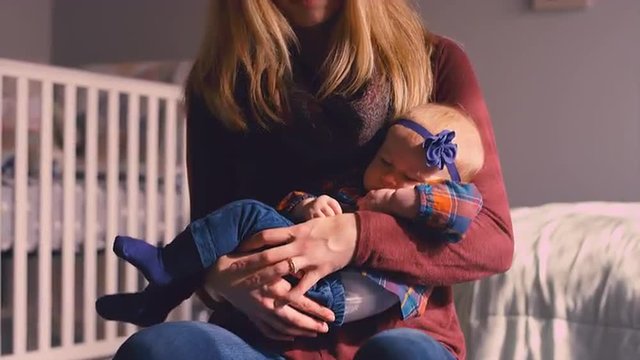 A young mother bouncing her baby to sleep on a yoga ball in a nursery