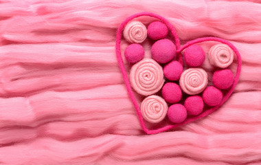 The contour of the heart as a valentines. Filled with beads and a stylized roses made of wool in different shades of pink. Background made of wool for felting
