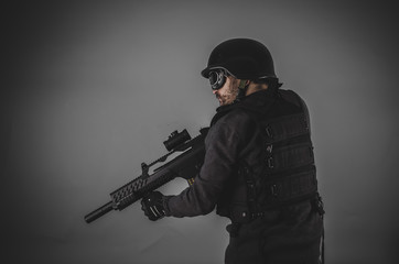 airsoft player with gun, helmet and bulletproof vest on gray bac
