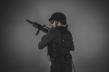 airsoft player with gun, helmet and bulletproof vest on gray bac