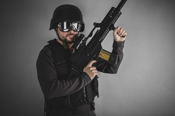 airsoft player with gun, helmet and bulletproof vest on gray bac