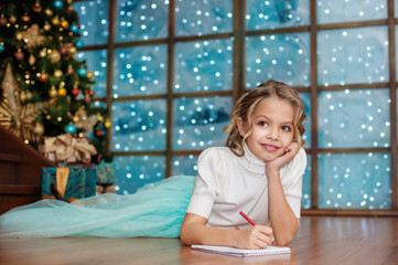 Little girl writes letter to Santa near christmas tree