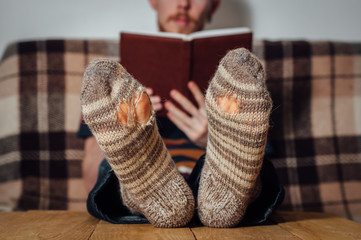 Young man reading book on coach in holey socks