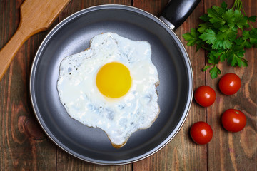 Pan of fried eggs, with cherry-tomatoes and parsley on a wooden table surface