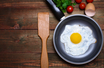 Pan of fried eggs, with cherry-tomatoes and parsley on a wooden table surface