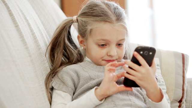 Cute little girl playing with smartphone at home