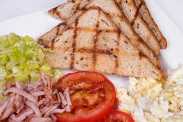 Traditional English breakfast with scrambled eggs, tomatoes, potatoes, toast and fresh salad