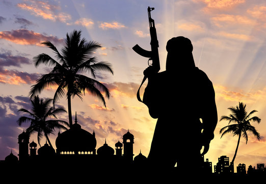 Silhouette of man with rifle near mosque during sunset