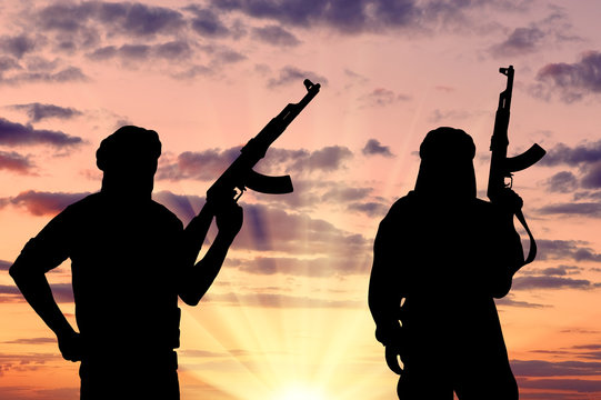 Silhouette of men with rifle against cloudy sky during sunset