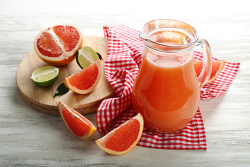 Jar of citrus juice and fresh fruits on light wooden background
