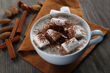 Cup of hot cacao with marshmallow, cinnamon and nuts on brown cotton serviette, close up