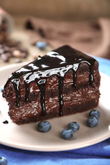 Chocolate cake with chocolate cream and fresh blueberries on plate, on wooden background