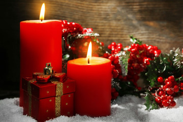 Burning candles, rowan and gift box with snow on wooden background