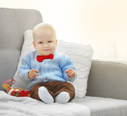 Funny baby sitting on sofa and Christmas tree on background