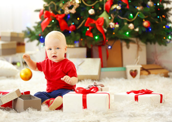 Funny baby with gift boxes and Christmas tree on background