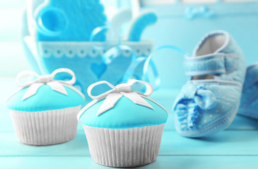 Tasty cupcakes with bow and baby shoes, decorative baby carriage and photo album  on color...