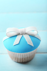 Tasty cupcake with bow on color wooden background